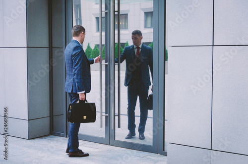 serious man in a suit with a briefcase hurries to a meeting in the business center. Businessman opens office door. Business life in the city.