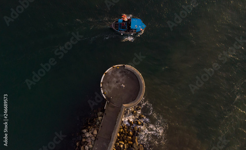 Aerial view of the pier at the harbor or Helsingborg, Sweden as a small fishing boat is leaving the calm waters for its work with catching fish. © Viktorishy