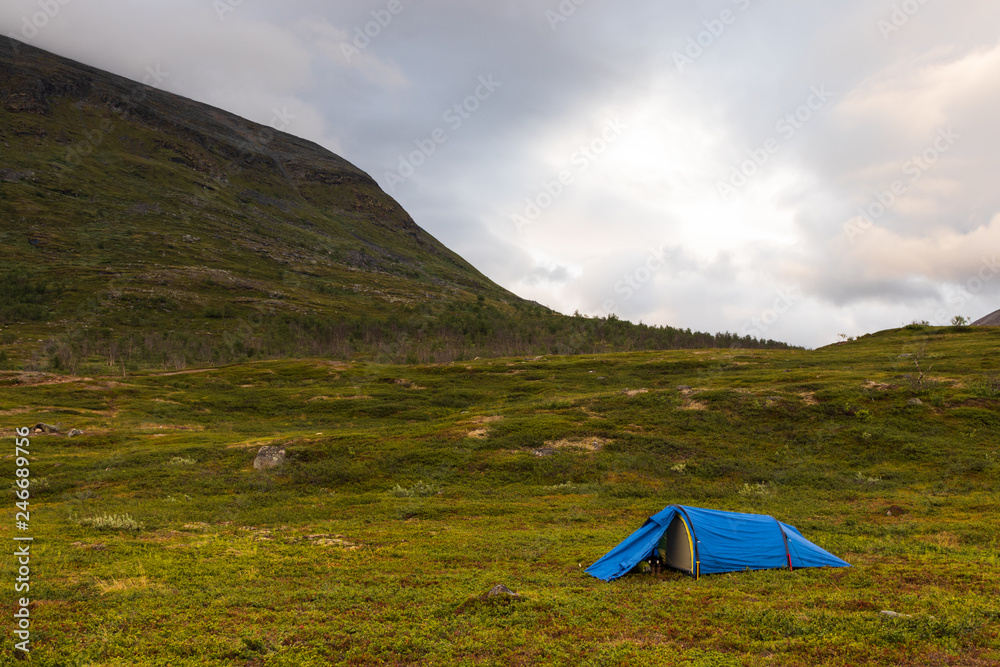 Tent standing on grass below a mountain making up a camp for hikers doing the Kungsleden (Kings trail) trail in northern Sweden. Shot just before sunset in summer. 