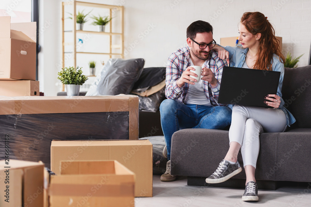 Young couple moving in new home. Sitting and relaxing after unpacking. Searching home decorating ideas on laptop. Online shopping. Young couple moving in new home. Sitting and relaxing after unpacking. Searching home decorating ideas on laptop. Online shopping.