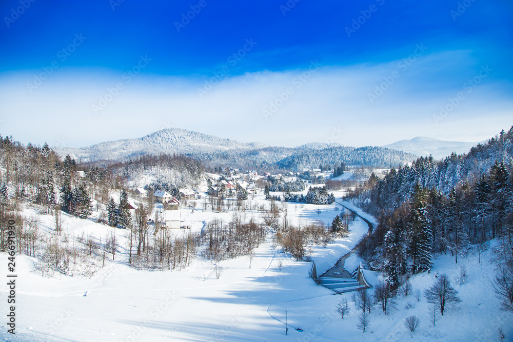 Croatian countryside landscape in winter, panoramic view of small town of Lokve under snow in Gorski kotar, mountains in background 