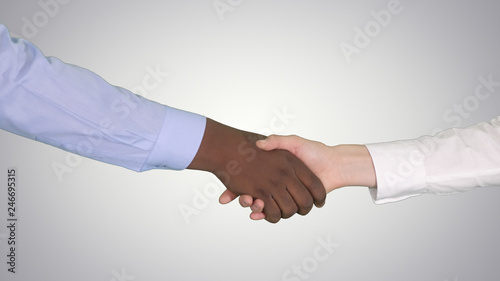 Handshake of Afro American and caucasian female hands on gradient background.