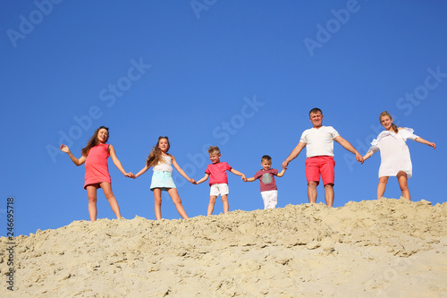 family with children stands holding hands on a sandy hill