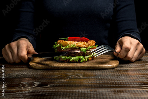 Healthy lifestyle  proper nutrition. Female hands are holding cutlery over a useful rice burger with vegetables  herbs and cutlet on a wooden board