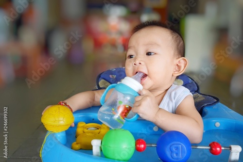 Asian baby drinking water and milk from baby milk bottle by herself. She sitting in a baby chair. 