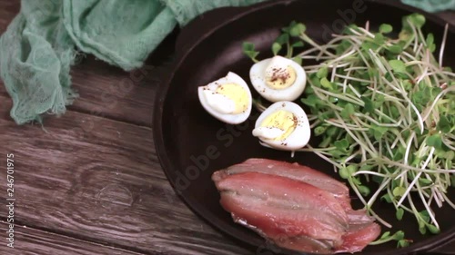 Unusual salad with leek sprouts, quail eggs and anchovies served in cast-iron pan