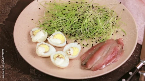 Unusual salad with leek sprouts, quail eggs and anchovies in plate on dark concrete background