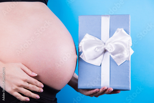 Wallpaper Mural Pregnant woman is holding festive gift box in her hand near belly on blue background. Torontodigital.ca