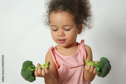 Cute African-American girl with broccoli on white background