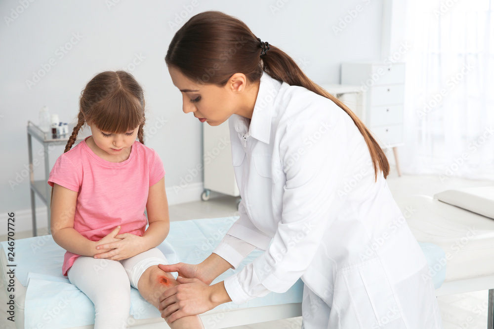 Female doctor examining little girl's injured leg in clinic. First aid Female doctor examining little girl's injured leg in clinic. First aid