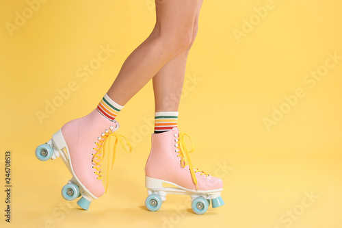 Young woman with retro roller skates on color background, closeup