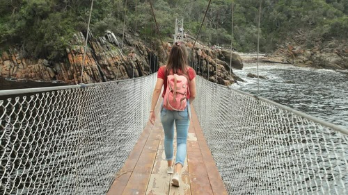 Girl walking over suspension bridge in a beautiful nature park. 
Shot on a Glidecam in 4k at 60fps so it can be slowed down if desired.