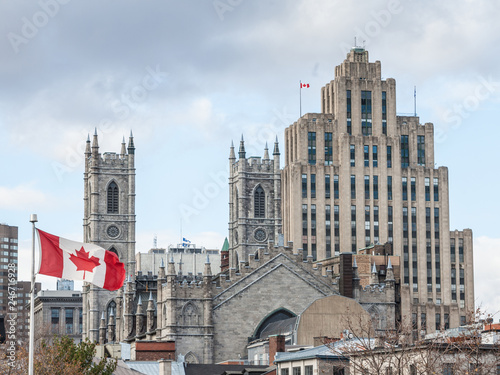 Skyline of Old Montreal, with Notre Dame Basilica in front, a vintage stone Skyscraper in background & a Canadian flag waiving. The basilica is the main cathedral of Montreal, Quebec, Canada