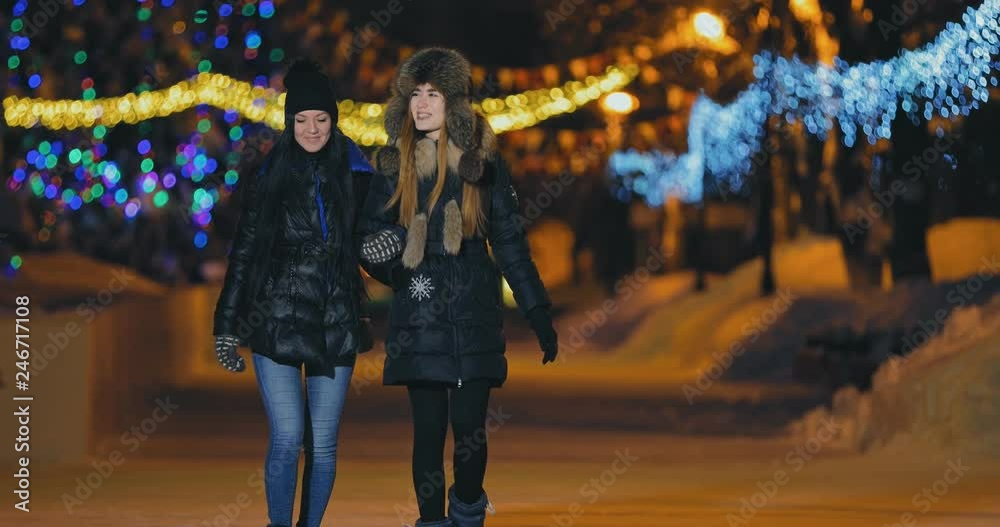 Pretty girls walk in the winter. Girlfriends talk and laugh. Street is beautifully decorated with garlands of lights.