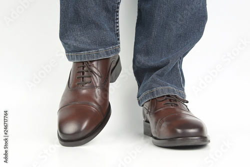 Male legs in jeans and brown classic shoes on white background