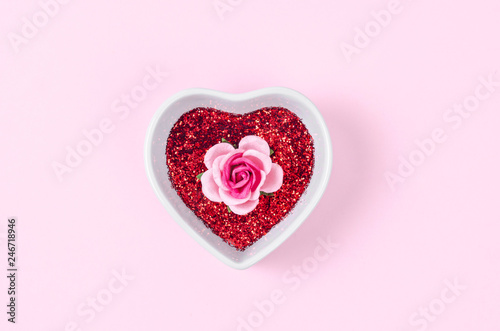 Pink rose and red glitter in white heart shaped bowl.