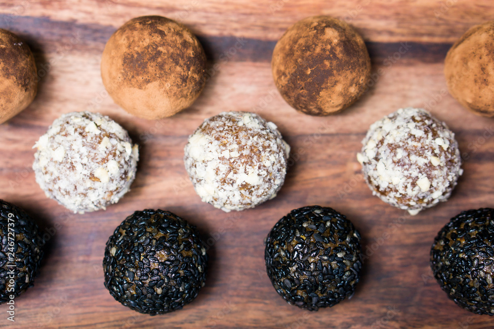 Flat lay of raw dates, oats, linseed and chia seed energy balls rolled in black sesame, chopped cashew nuts and cacao powder