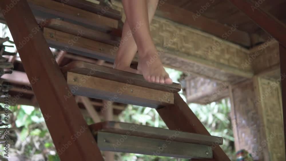 Close up detail view of bare female feet step down wooden stairs, fine barefoot legs, girl goes down in tropical house Close up detail view of bare female feet step down wooden stairs, fine barefoot legs, girl goes down in tropical house