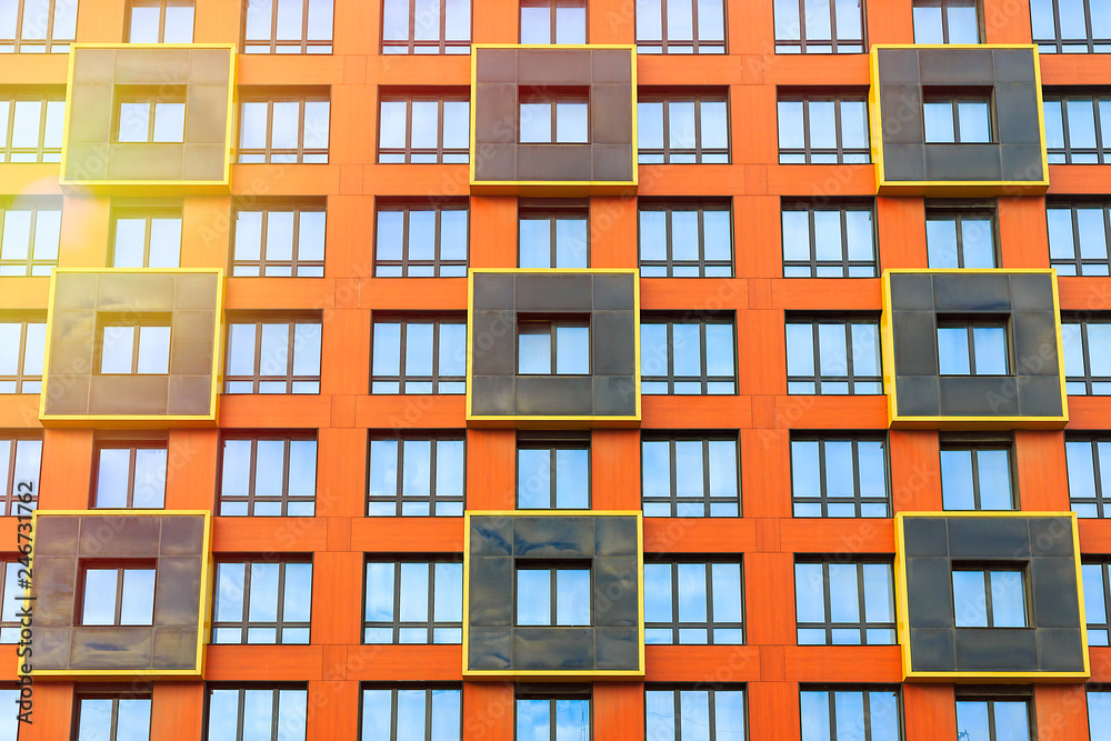 The facade of a modern high-rise building. Front view of many windows. Black squares with a yellow border against a bright orange wall. Perfect for urban background and design.