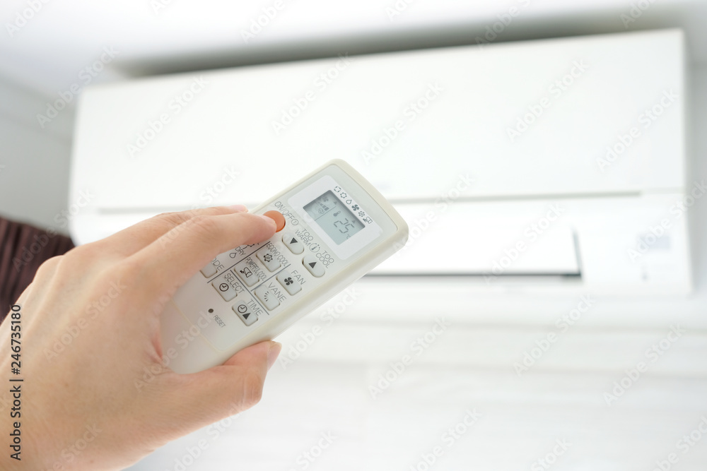 Man's hand using remote control open The air conditioner is cooled to 25 degrees Celsius in his bedroom. Health concepts and energy savings