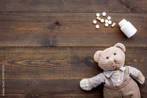 Childhood diseases concept. Treatment of children.Teddy bear toy and pills on dark wooden background top view space for text