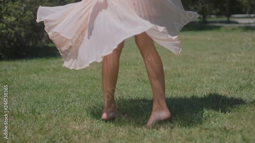 slow motion low angle shot girl barefoot figure dances spinning and pink dress skirt fans on summer park green grass