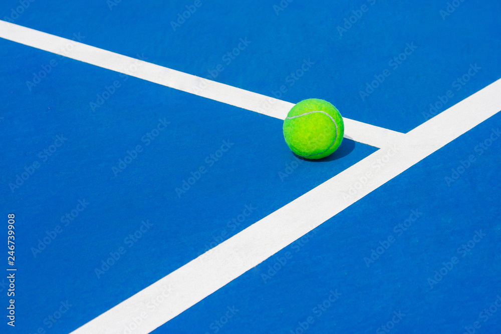 Green ball falling on floor nearly white lines of outdoor blue tennis hard court in public park. (Selective focus)