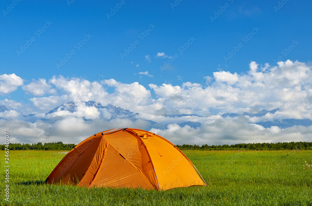 The orange tent on the meadow with foggy mountains on background