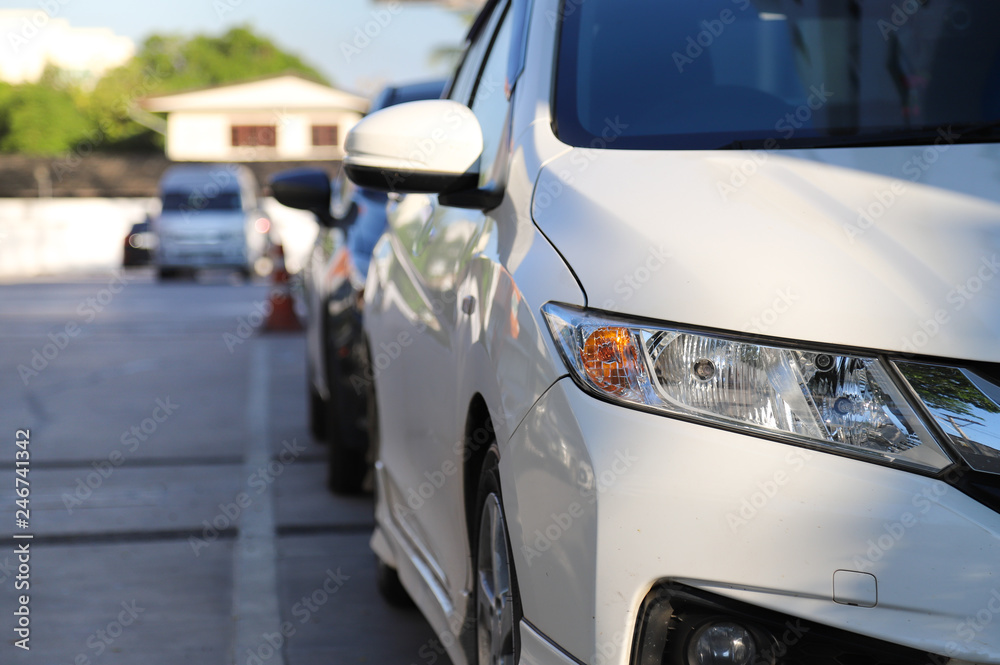 Closeup of front side of white car parking in parking area with natural background in the morning of sunny day.