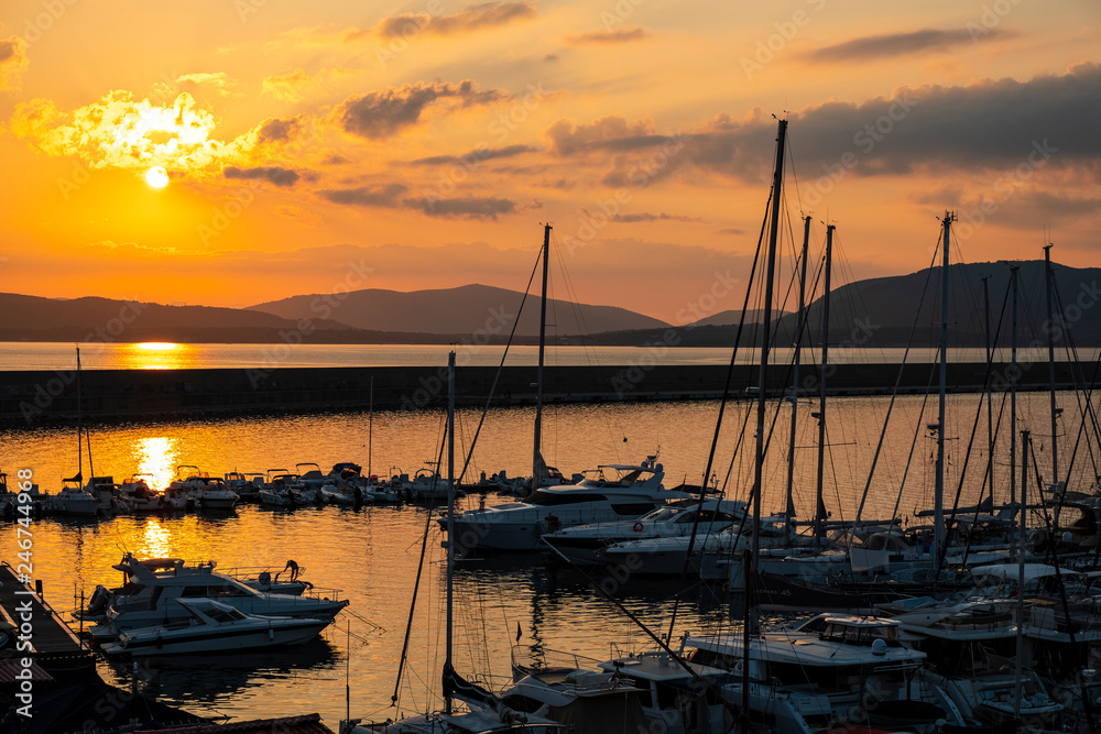 Alghero, Sardinia, Italy - Summer sunset skyline over the Alghero Marina yacht port at the Gulf of Alghero at Mediterranean Sea
