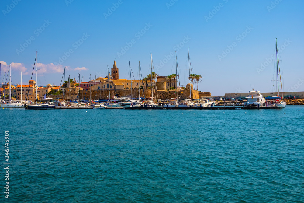 Alghero, Sardinia, Italy - Summer view of the Alghero Marina yacht port at the Gulf of Alghero at Mediterranean Sea with the Old Town quarter with historic defense walls