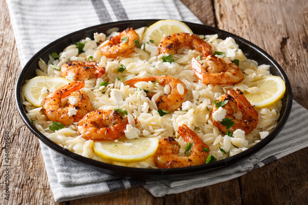 Main course orzo pasta with shrimps, feta cheese, herbs and lemon close-up on the table. horizontal