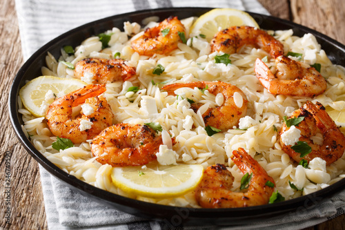 Spicy orzo pasta with grilled shrimps, feta cheese, herbs and lemon close-up on a plate. horizontal