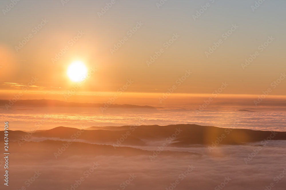 Fototapeta premium Beautiful sunset over a valley filled by fog with mountains and hills
