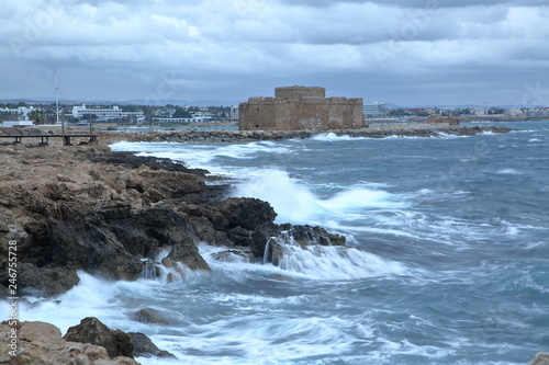 Landscape with rocky coastlie in pafos, Cyprus, sea with waves, historical fortress, town on horizon, long exposure