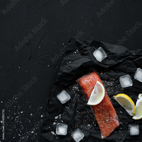 Salmon steak on black background with lemon, ice and seasonings.Copy space.Top view.