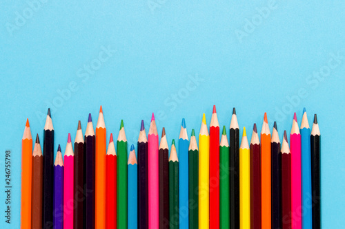 Color pencils laid out in the form of a wave on a blue background. Flat lay, top view