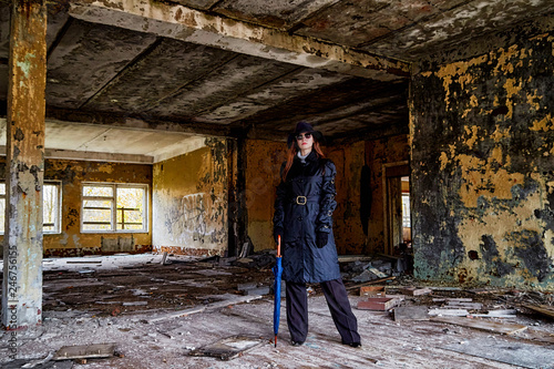 Girl in a black cloak and hat posing in an abandoned, ruined house. Unusual photo shoot