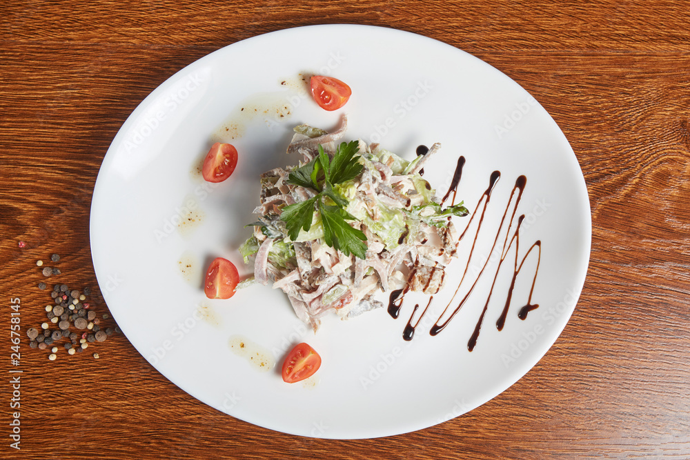 beef tongue in a salad with pork tenderloin, pickles, parsley and lettuce, decorated with cherry tomatoes and soy sauce, next to a plate filled with pepper seeds beef tongue in a salad with pork tenderloin, pickles, parsley and lettuce, decorated with cherry tomatoes and soy sauce, next to a plate filled with pepper seeds