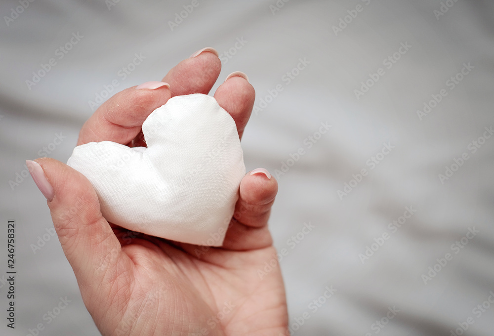 white handmade fabric heart in woman's hand in grey background white handmade fabric heart in woman's hand in grey background