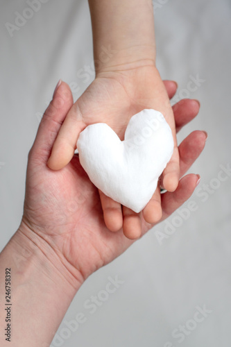 image of two hands holding white fabric heart. Mother and child together