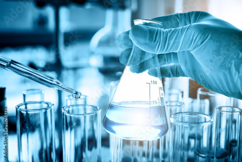 hand of scientist holding flask with lab glassware in chemical laboratory background, science laboratory research and development concept 