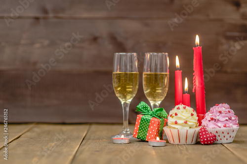 Fototapeta Naklejka Na Ścianę i Meble -  Pair glass of champagne with cupcakes, gift box and candles. Wooden background with empty space for text