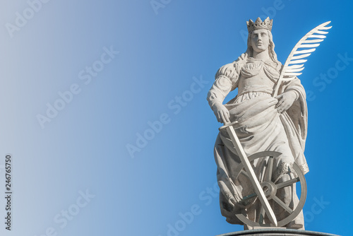 Statue of Catherin with writing bird feather, sword and cartwheel at ancient portal in Magdeburg, Germany, closeup, gradient blue sky photo