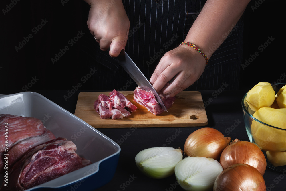 Female chef cutting meat for potato baked pudding with meat on black wooden table, hands, close up. Selective focus.