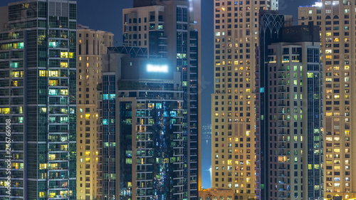 Glowing windows in multistory modern glass and metal residential buildings light up at night timelapse.