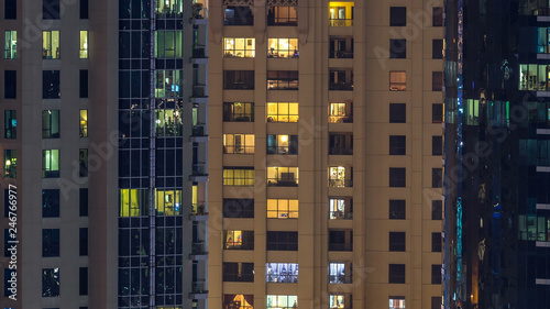 Glowing windows in multistory modern glass and metal residential building light up at night timelapse.