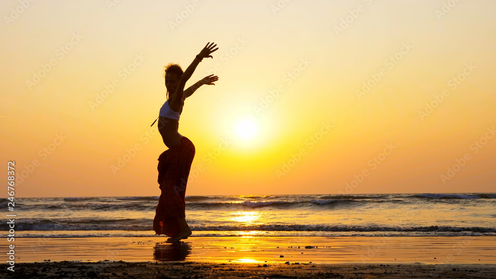 Silhouette of young girl dancing on the beach at sunset