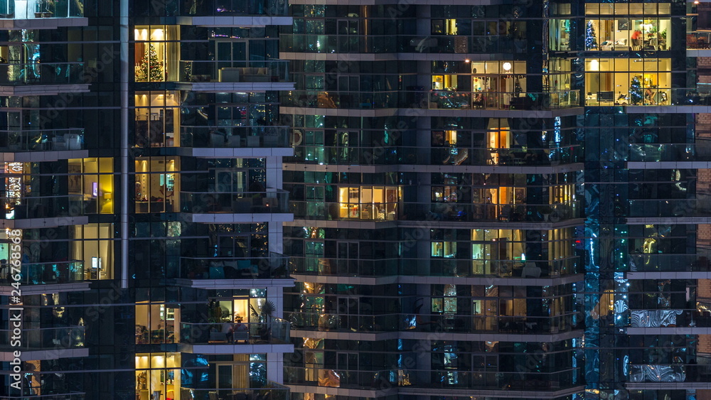 Glowing windows in multistory modern glass residential building light up at night timelapse.