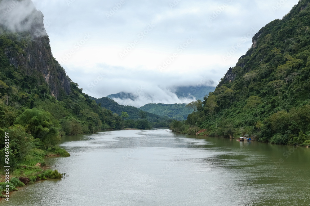 Nam Ou river view with small long boat sailing. A valley surrounded by steep limestone cliffs covered with jungle. Image taken in Nong Khiaw - a village in the Luang Prabang Province of northern Laos.